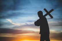 silhouette of a man holding up a cross at sunset 