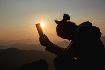 Silhouette of a woman praying with her Bible at sunset