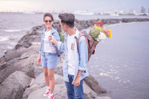 a couple standing on a jetty with flowers in their backpacks 