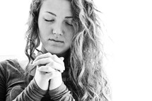 Teenage girl praying with fingers laced.