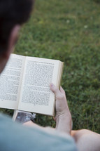 man reading a book in the grass 