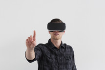 A man wearing virtual reality glasses and holding his finger up.