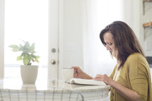 woman sitting at a kitchen table reading a Bible 