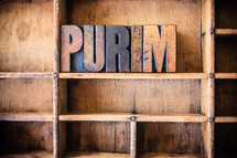 Wooden letters spelling "purim" on a wooden bookshelf.