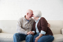 a happy, loving elderly couple snuggling on a couch 
