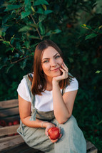 Woman with red juicy apple from tree in own home countryside orchard. Happy gardener, young farmer style. Healthy lifestyle. High quality