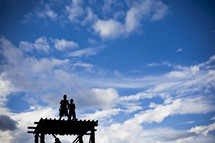boys standing on a roof under white clouds in a blue sky