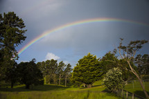 A rainbow arching across a field of green and trees.