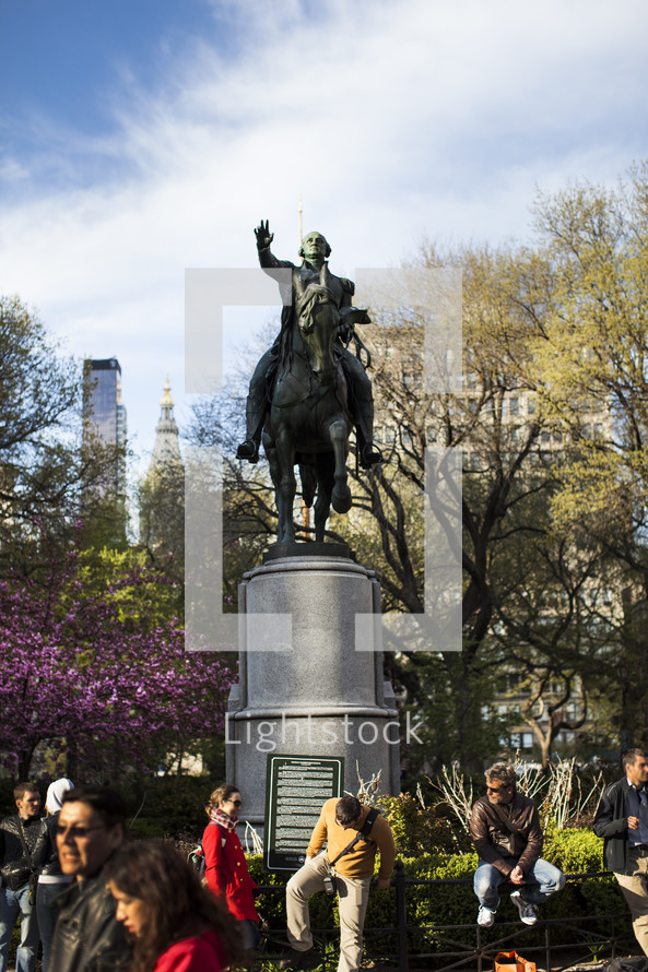 Bronze statue of a man on a horse in a crowded park.