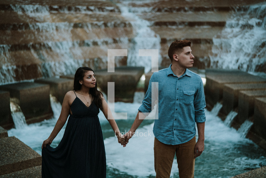 a couple holding hands standing on a fountain 