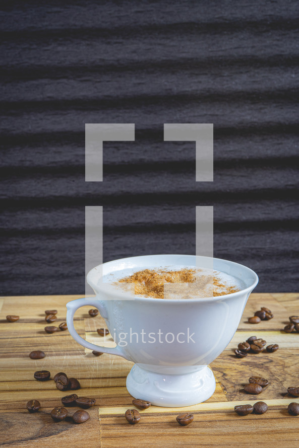 Delicious home made Cappuccino, in a white cup, on a wooden table. With coffee beans. Home made Coffee.