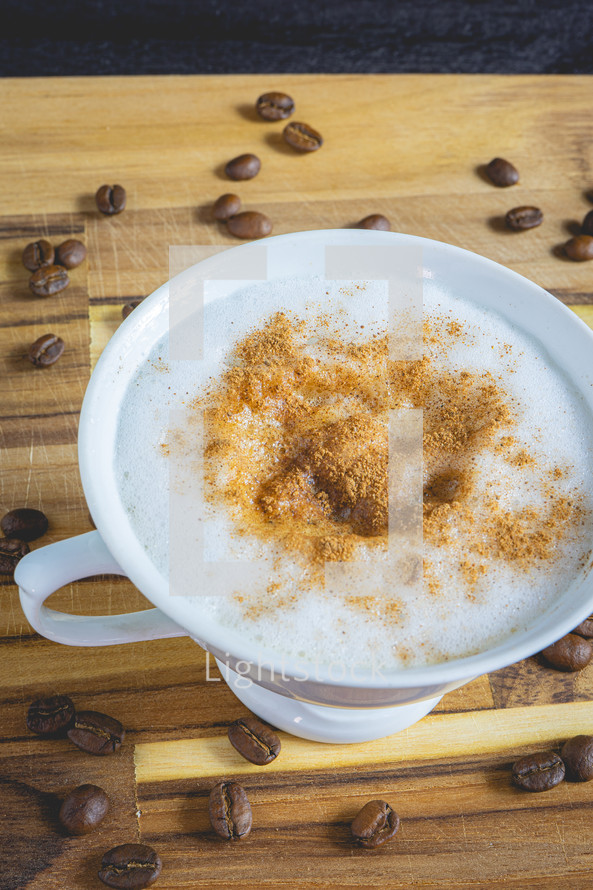 Delicious home made Cappuccino, in a white cup, on a wooden table. With coffee beans. Home made Coffee.