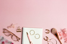 notebook, and makeup on a pink background 