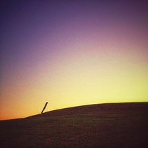 Person leaning forward on top of hill at sunset.