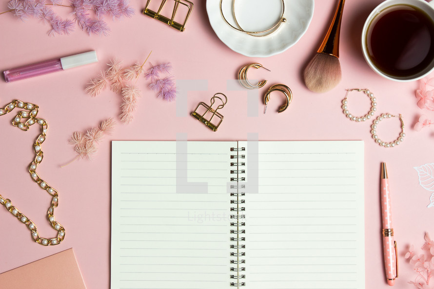 coffee cup, notebook, and makeup on a pink background 