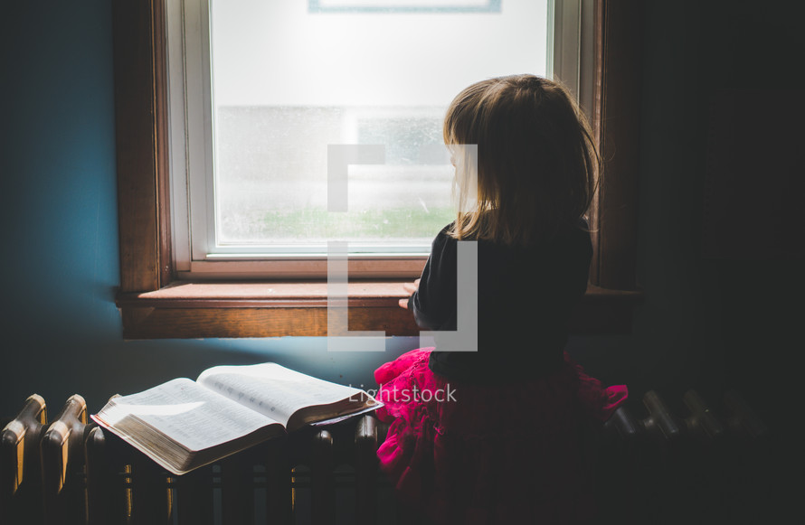 a girl looking out a window and an open Bible 
