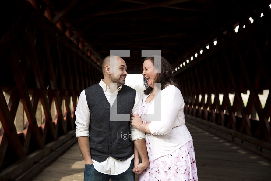 Man and woman laughing together on a covered bridge.
