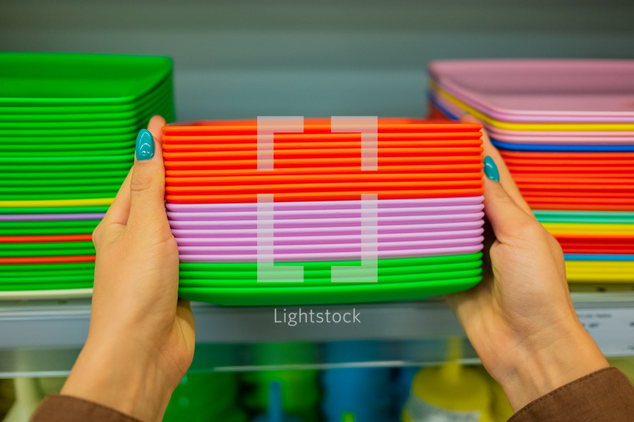 Woman chooses plates. Simple pop of colors. Shelf in a store with brightly colored kitchen utensils