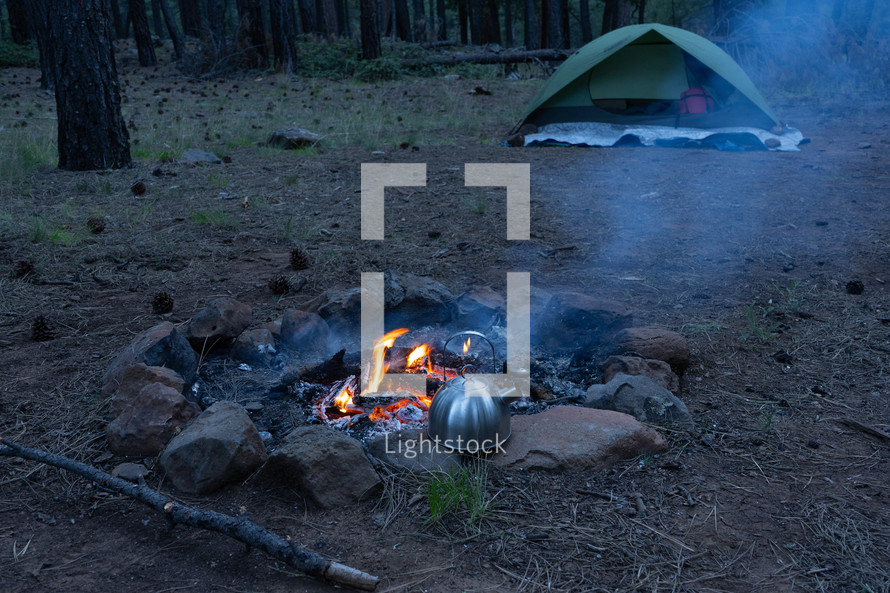 Campfire and tent at a campsite in the forest