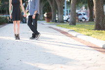 a couple holding hands standing on a sidewalk outdoors 