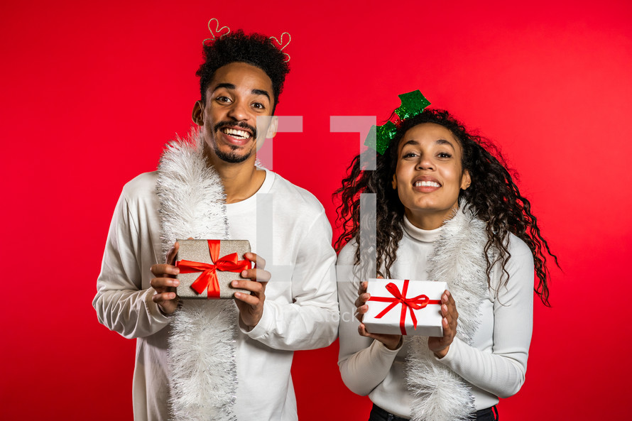 Young african american couple with christmas gift box isolated on red background studio. New 2025 year decorations, presents, party, happiness concept. High quality photo