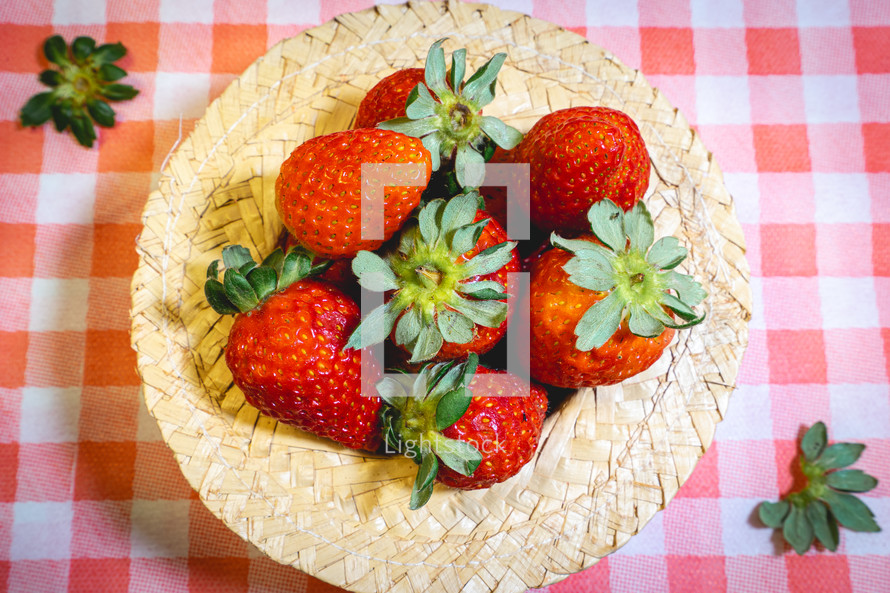 Fresh strawberries decorated on a straw hat. on a red picnic blanket.