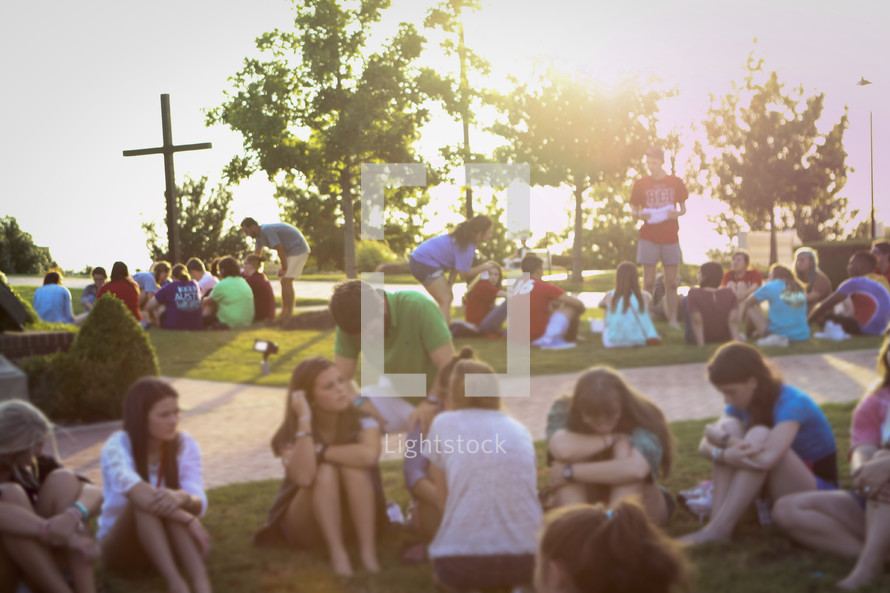 youth sitting in the grass outdoors around a cross 
