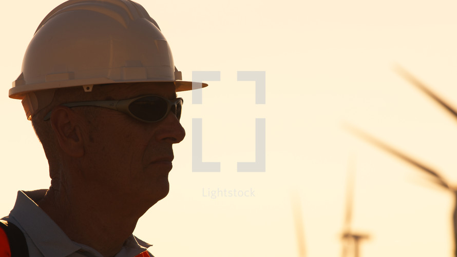 Silhouette of an engineer with white helmet in wind farm