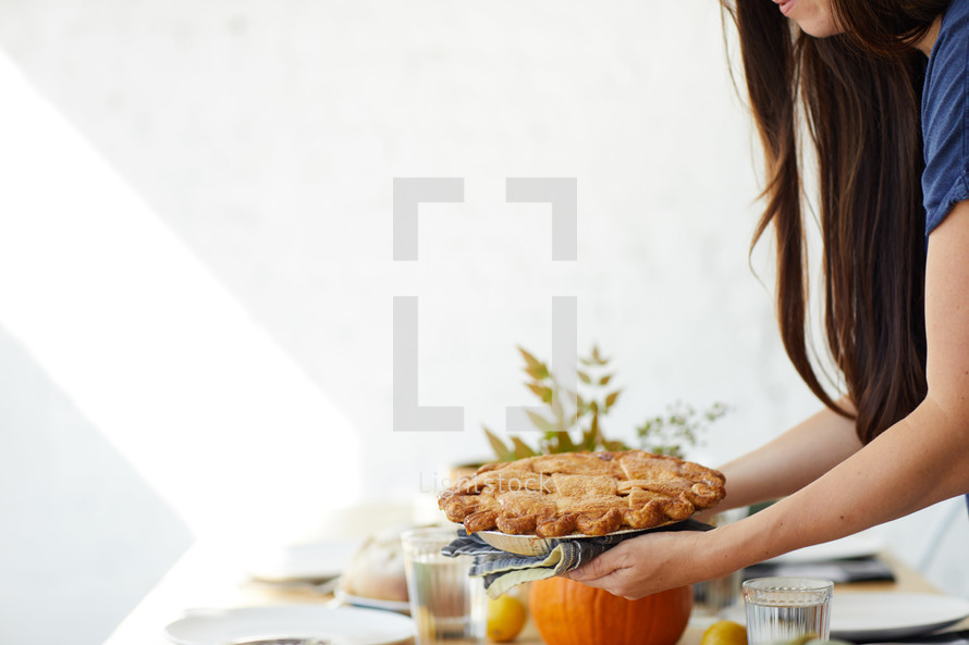 a woman putting a pie on a thanksgiving table 