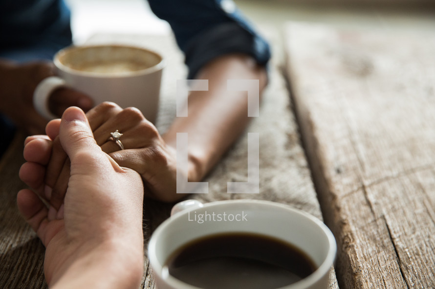 a couple holding hands and mugs 