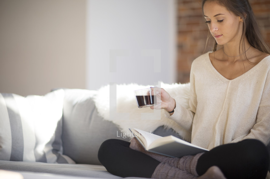 a woman sitting on a couch reading holding a coffee cup 