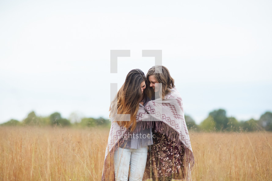 friends wrapped in a blanket standing in a field 