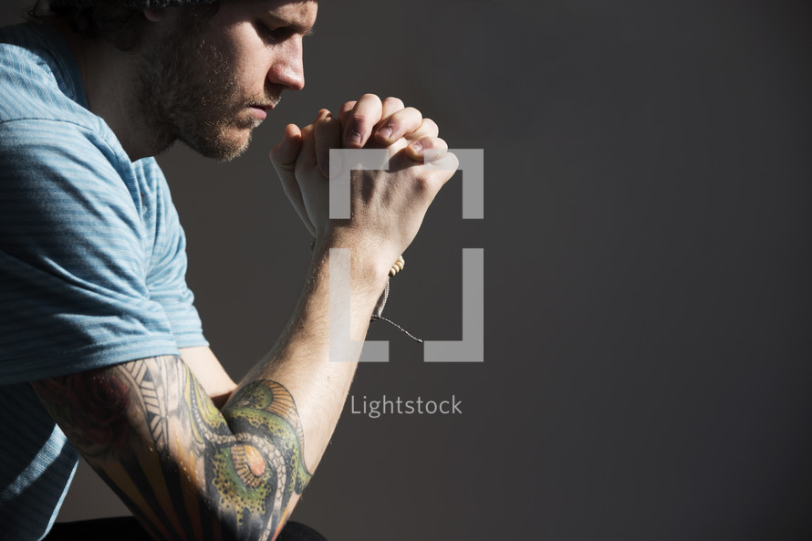 a man with a sleeve tattoo praying.