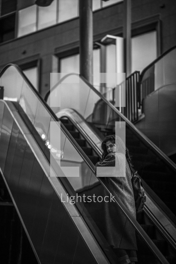 a woman in a trench coat on an escalator 
