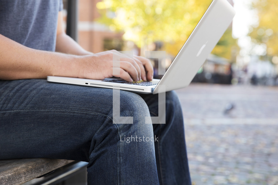 man sitting on bench while typing on his laptop