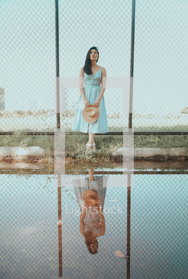 woman in a dress holding a hat and reflection in water 