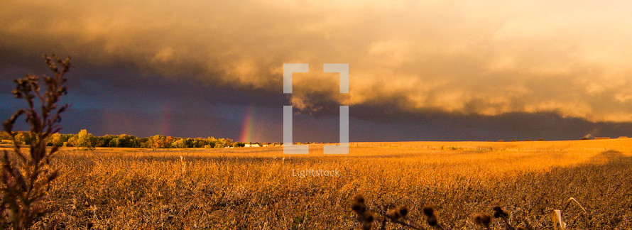 weather front over a field and a rainbow
