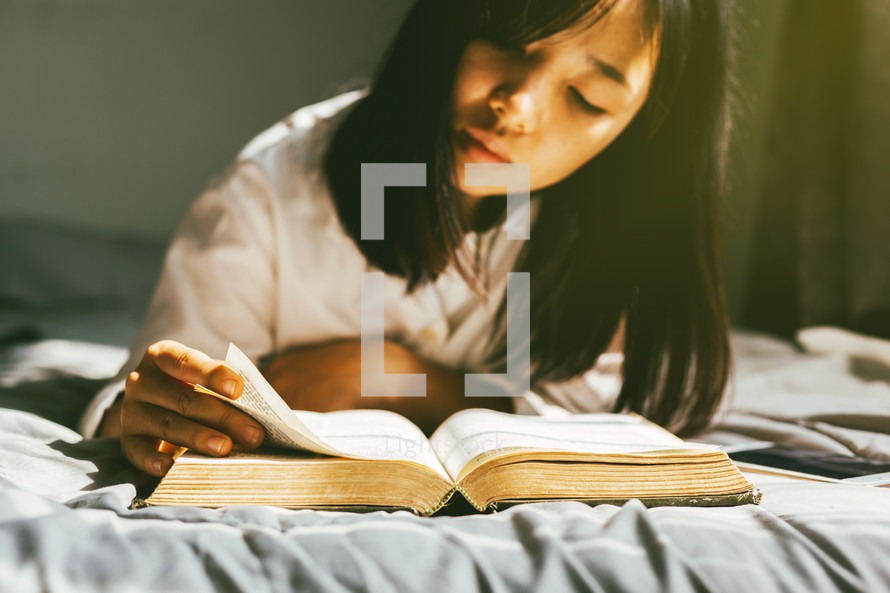 a girl reading a Bible in bed 