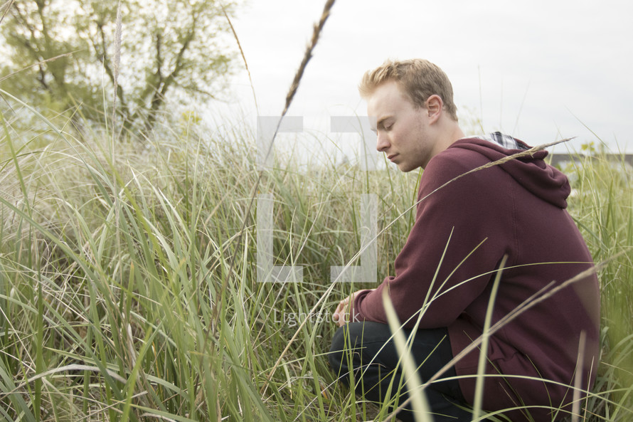 a man sitting in tall grass and praying quietly