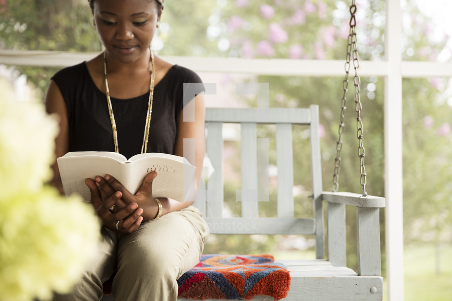 Woman sitting outside on a porch swing reading the Bible.