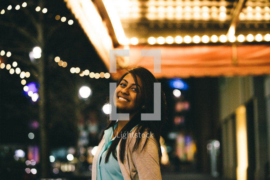 Smiling woman standing outside under a marquee of lights.
