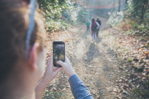woman taking a picture with her cellphone of a group hiking on a nature trail 