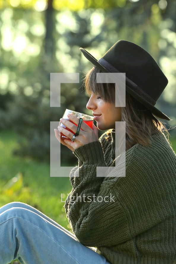 Young Woman in a hat Holding a Hot Tea Cup outdoors in fall 