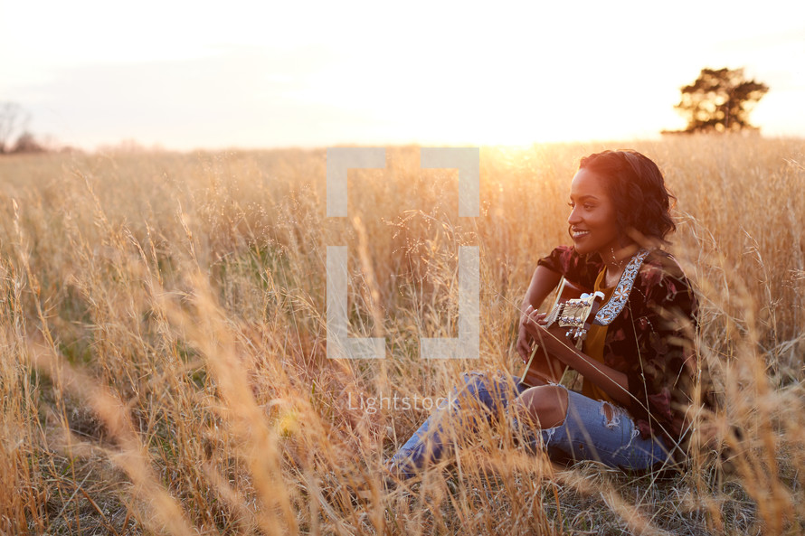 a woman sitting in a field with a guitar 
