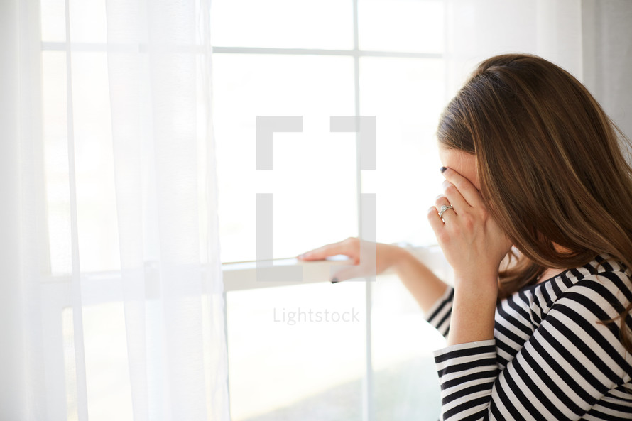a woman standing in front of a window crying 
