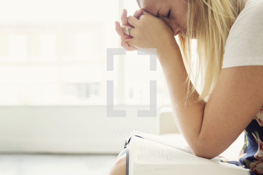 woman sitting on a couch with a Bible in her lap praying 