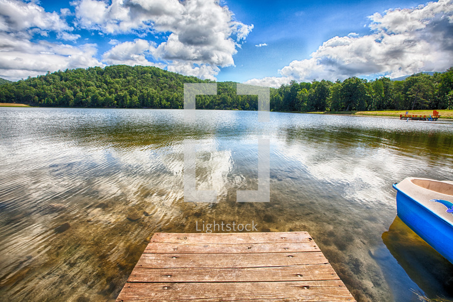 Pier on a crystal clear lake with trees and clouds on the horizon.