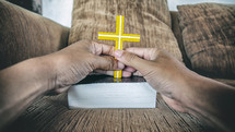 hands holding a cross over a Bible in prayer 