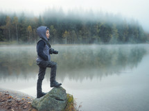 Creative child, kid photographer (a little boy) with a camera taking landscape pictures near a lake