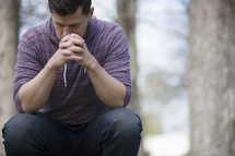 a man with head bowed in prayer outdoors 